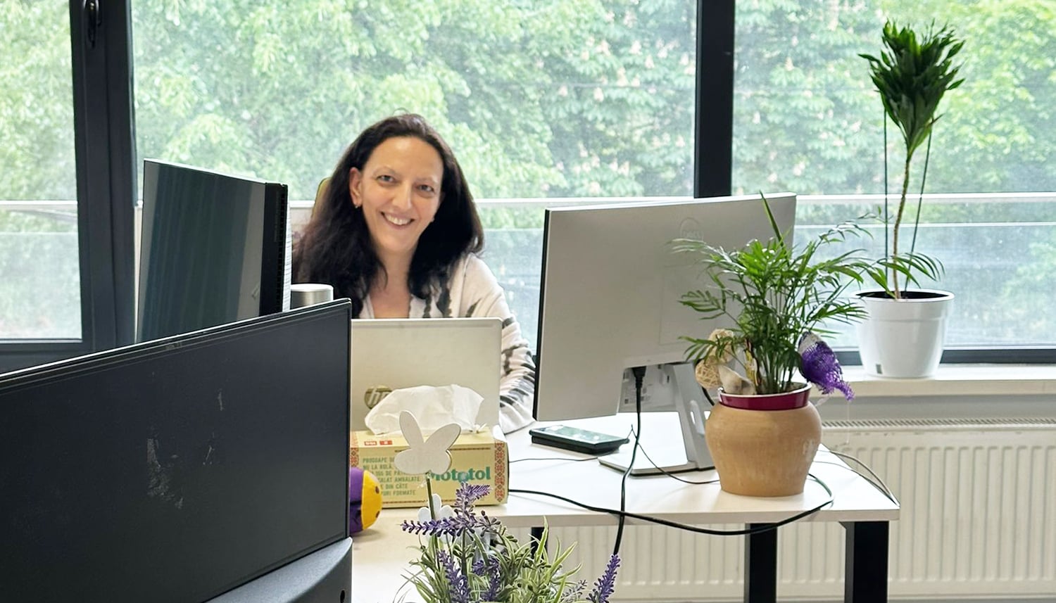 Colegă Spring FARMA zâmbind la birou, în fața a două monitoare